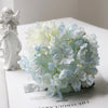 A bouquet of light blue and white hydrangea flowers displayed next to a white angel figurine.
