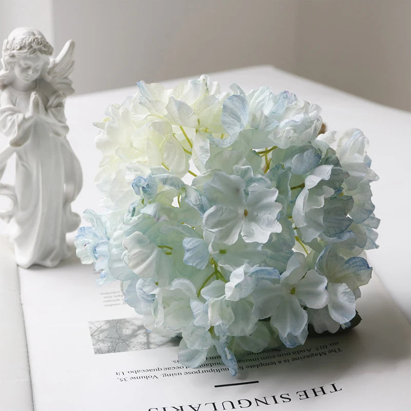 A bouquet of light blue and white hydrangea flowers displayed next to a white angel figurine.