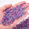 A hand holds a pile of mixed size crystal and glass rhinestones in various shades of purple and pink.