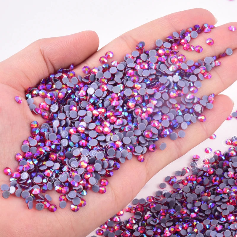 A hand holds a pile of mixed size crystal and glass rhinestones in various shades of purple and pink.