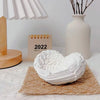 White resin sculpture shaped like angel wings forming a heart placed on a woven mat