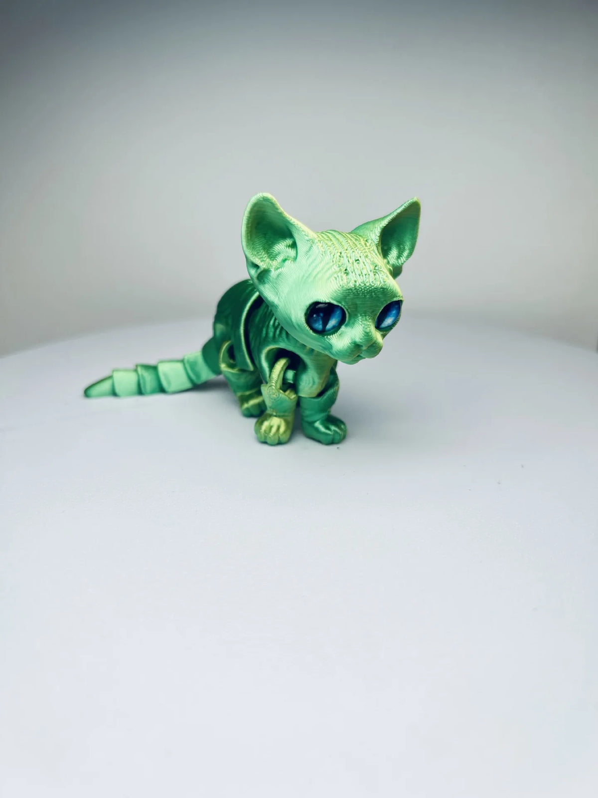 A green articulated 3D printed figurine of a Siamese cat with blue eyes.