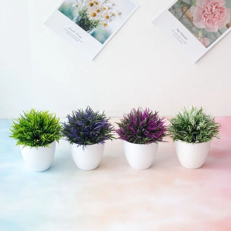 Trois bonsais artificiels en pots blancs avec feuillage vert et violet, présentés sur une surface rose.
