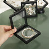 A hand opens a black display box to reveal a gold-toned pearl necklace inside.