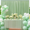A light green chiffon backdrop curtain decorated with white balloons and floral arrangements for an event.