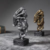 A set of three resin figurines depicting faces in silver and gold tones on a dark surface.