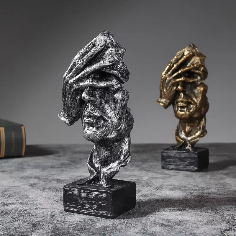 A set of three resin figurines depicting faces in silver and gold tones on a dark surface.