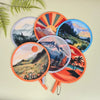 A collection of round, colorful hand-held cooling fans featuring scenic landscapes and sunburst designs.