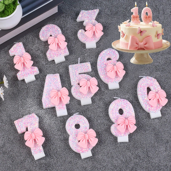 Glitter number cake candles from 0 to 9 with pink bows arranged on a gray surface.