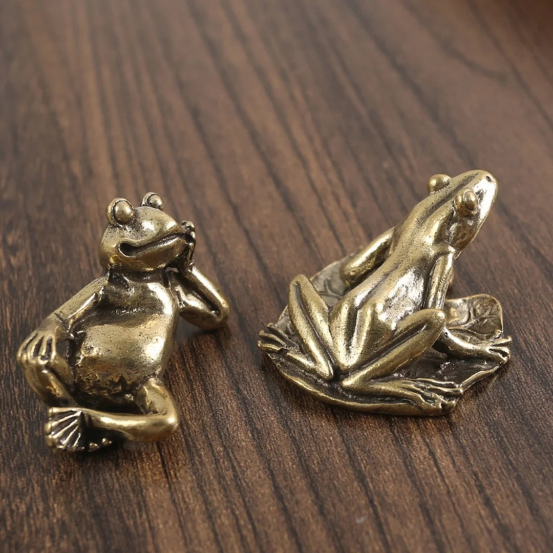Antique brass frog sculpture decor resting on a dark wooden surface.