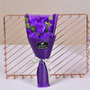 A purple handcrafted soap rose bouquet displayed in a glass vase on a copper wire rack.