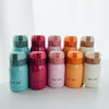 A row of eight compact stainless steel vacuum insulated coffee mugs in various shades of teal, pink, orange, and beige.