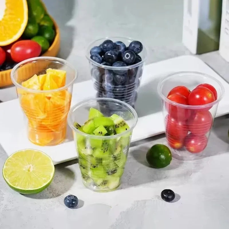 A collection of fresh fruit like oranges, berries, and lime slices displayed in clear plastic cups on a white surface.