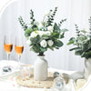 Ein Strauß weißer Blumen und grüner Eukalyptusblätter auf einer weißen Tischdekoration.