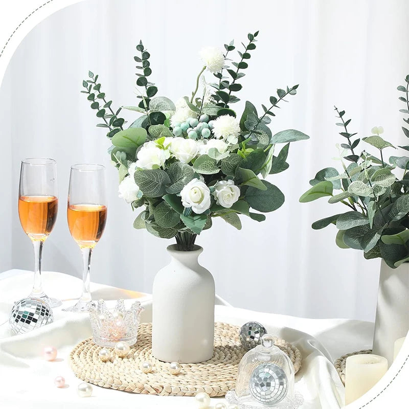 Ein Strauß weißer Blumen und grüner Eukalyptusblätter auf einer weißen Tischdekoration.