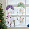 A hanging crystal tree of life sun catcher with purple and green elements displayed in a window