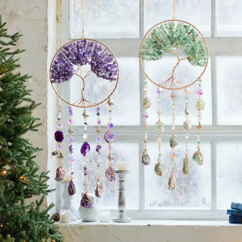 A hanging crystal tree of life sun catcher with purple and green elements displayed in a window
