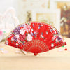 A vibrant red lace hand fan decorated with pink and purple floral patterns, resting on a light wooden surface.