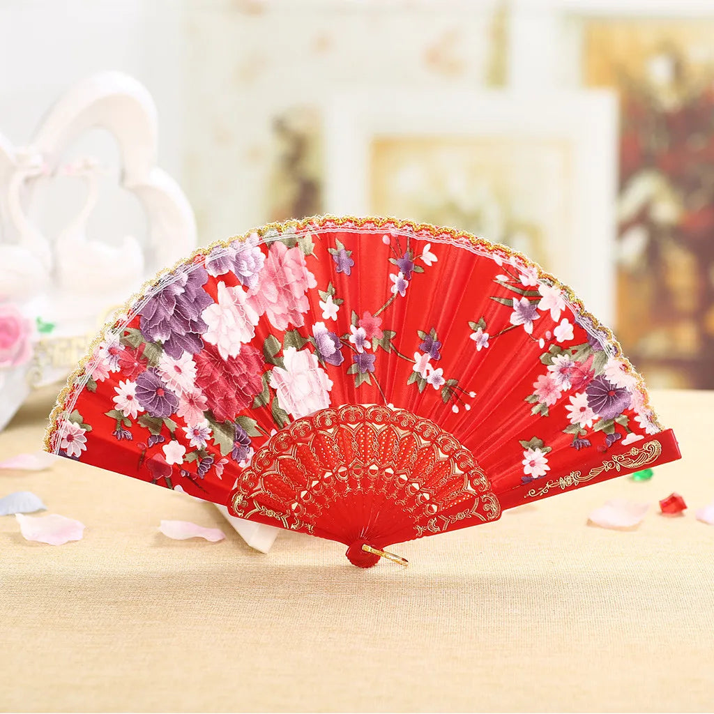 A vibrant red lace hand fan decorated with pink and purple floral patterns, resting on a light wooden surface.