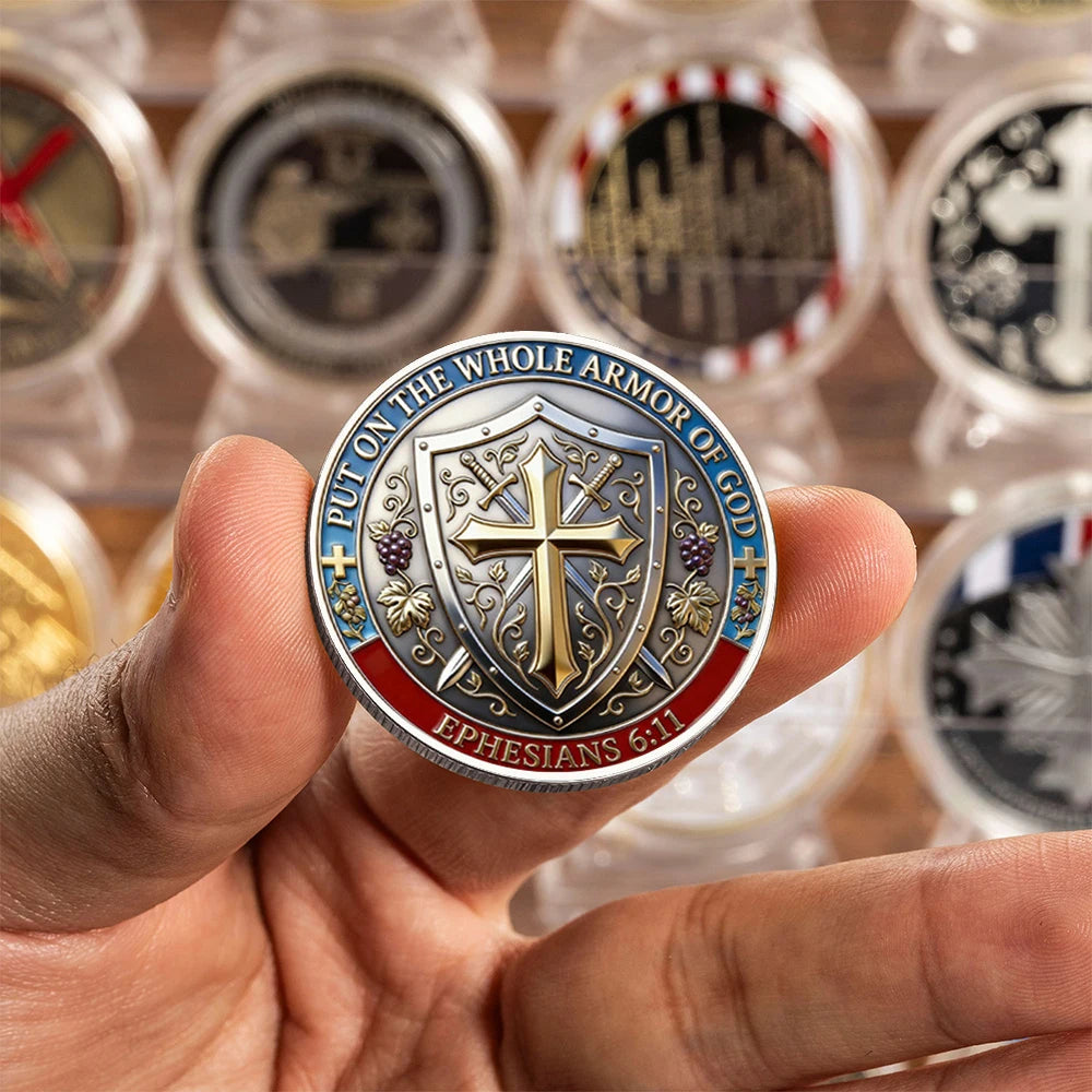 A hand holds a silver-plated commemorative coin featuring a cross design and the scripture Ephesians 6:11.