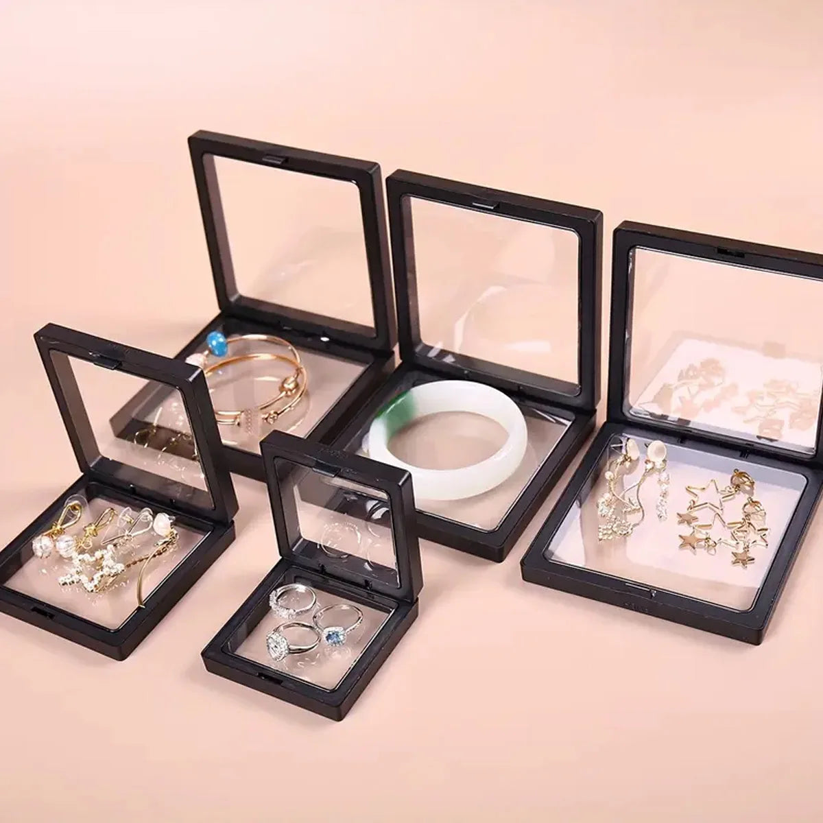 A set of black transparent floating display boxes for jewelry and collectibles, showing various rings and earrings.