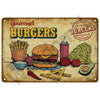 A vintage-style metal sign decoration featuring illustrations of gourmet burgers, french fries, vegetables, and a tomato.