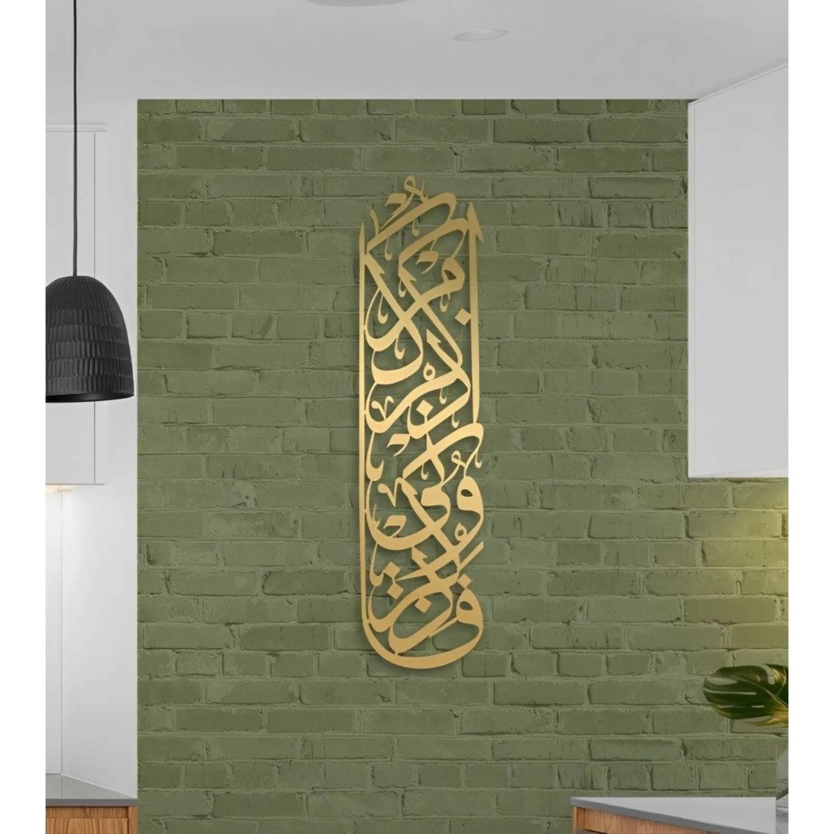Gold metal calligraphy of Bismillah mounted on a textured olive green brick wall.