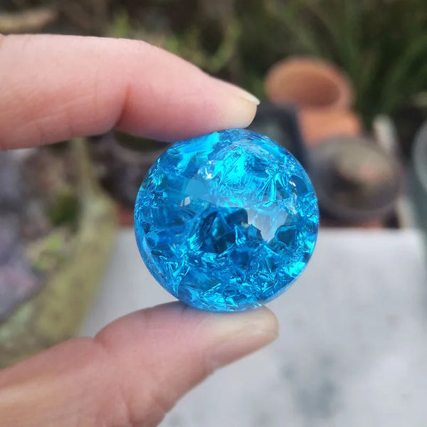 A hand holds a brilliant, deep blue crystal ice crack ball used as water fountain decor.