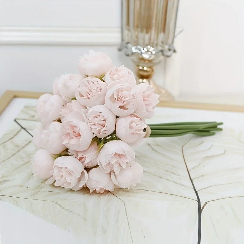 A bouquet of light pink silk peonies with green stems displayed on a white surface.