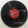 A black vinyl record is used as a decorative wall clock with an orange face and hands.