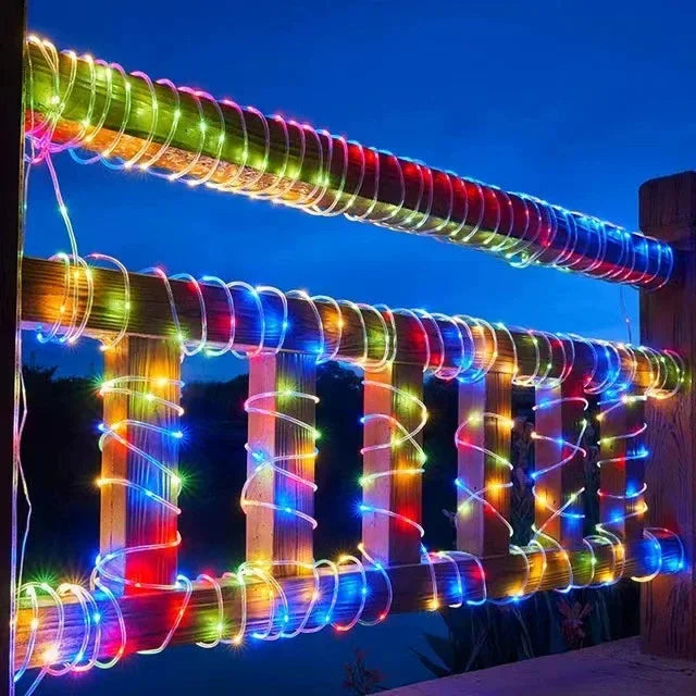 A long, colorful LED rope light is strung across a wooden fence at twilight.