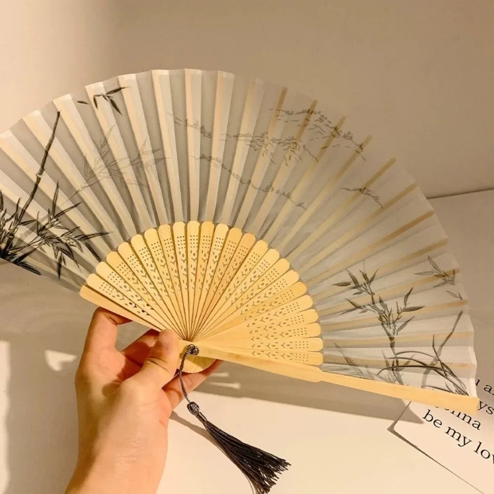 A hand is holding a light-colored folding fan with black accents and leaf patterns.