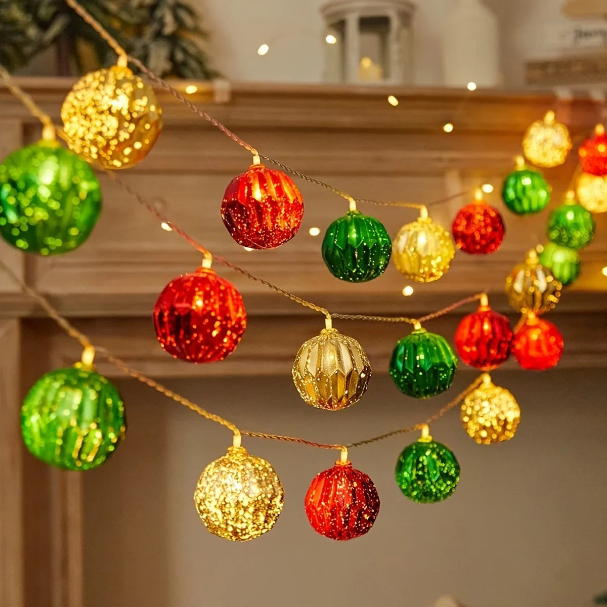 String lights with various colored gold and green ornaments hanging above a wooden mantelpiece.