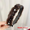 A hand holds a black hair band featuring dark brown braided hair and small pearl embellishments.