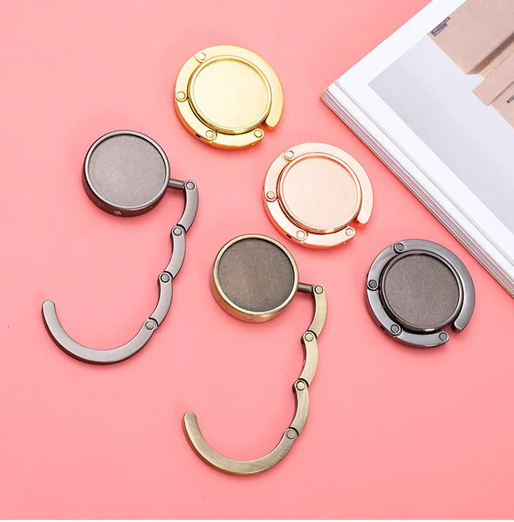 A collection of gold and silver compact folding table bag hooks or purse hangers arranged on a pink background.