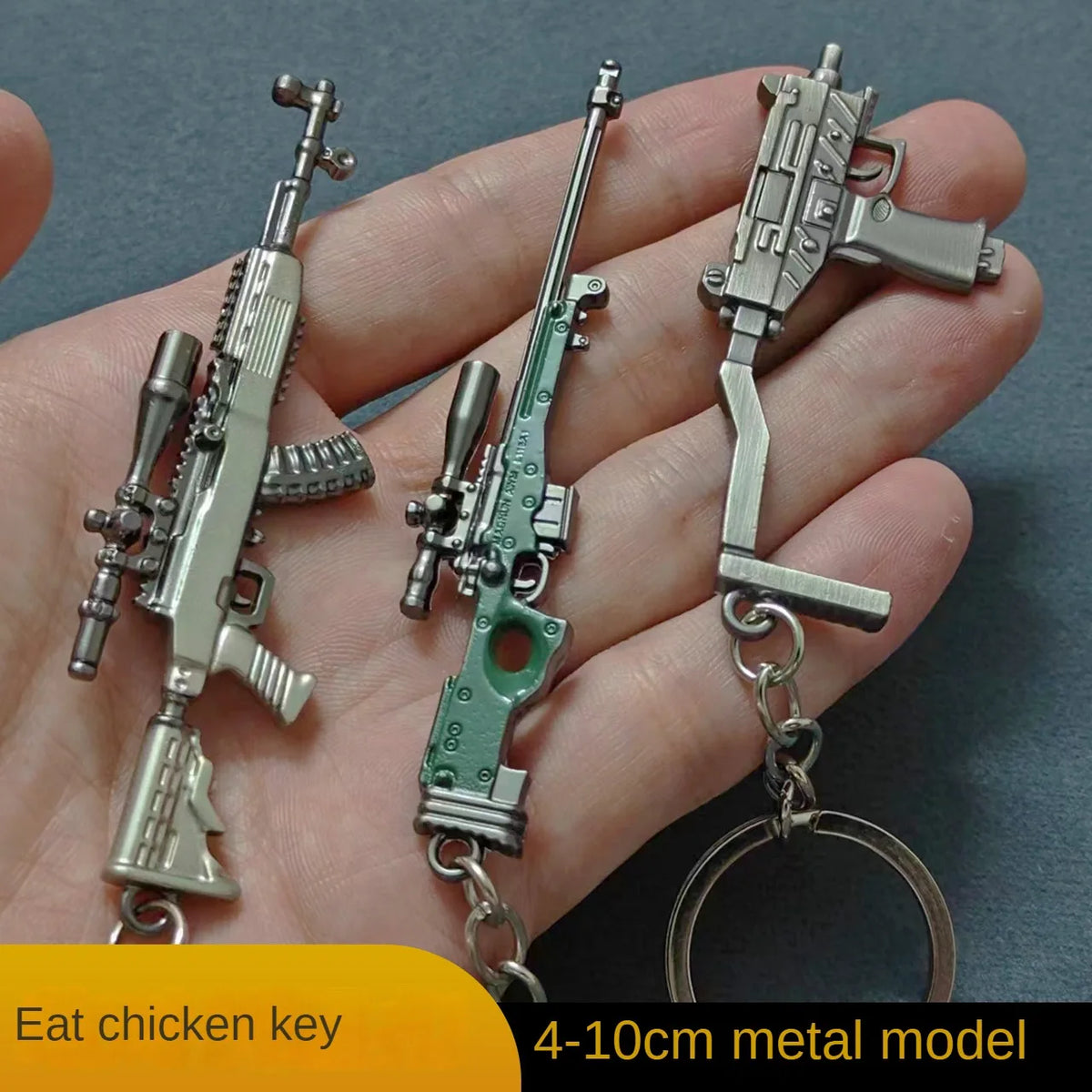 A hand holds an alloy gun model keychain featuring a realistic miniature firearm.