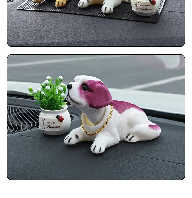 A white and pink dog ornament figure is shown resting on a dark gray surface next to a small potted plant.