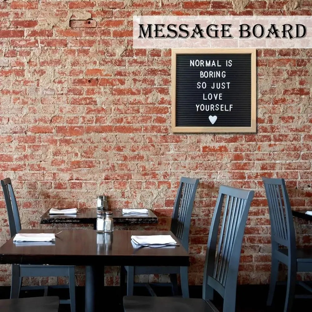 A wooden message board with text that reads Normal is boring so just love yourself mounted on a brick wall above a dark woode