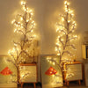 A decorative branch of willow vine lights illuminates a wooden cabinet and framed decor.