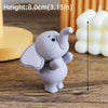 A small gray cartoon elephant cake topper is shown on a wooden surface next to a measuring scale.
