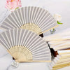A set of bridal handheld folding fans in light gray and natural wood tones displayed on a white marble surface.