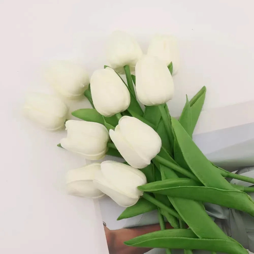 A bouquet of white artificial tulips with green stems and leaves.