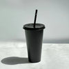 A black glitter party cup with a black lid and straw standing on a white surface.
