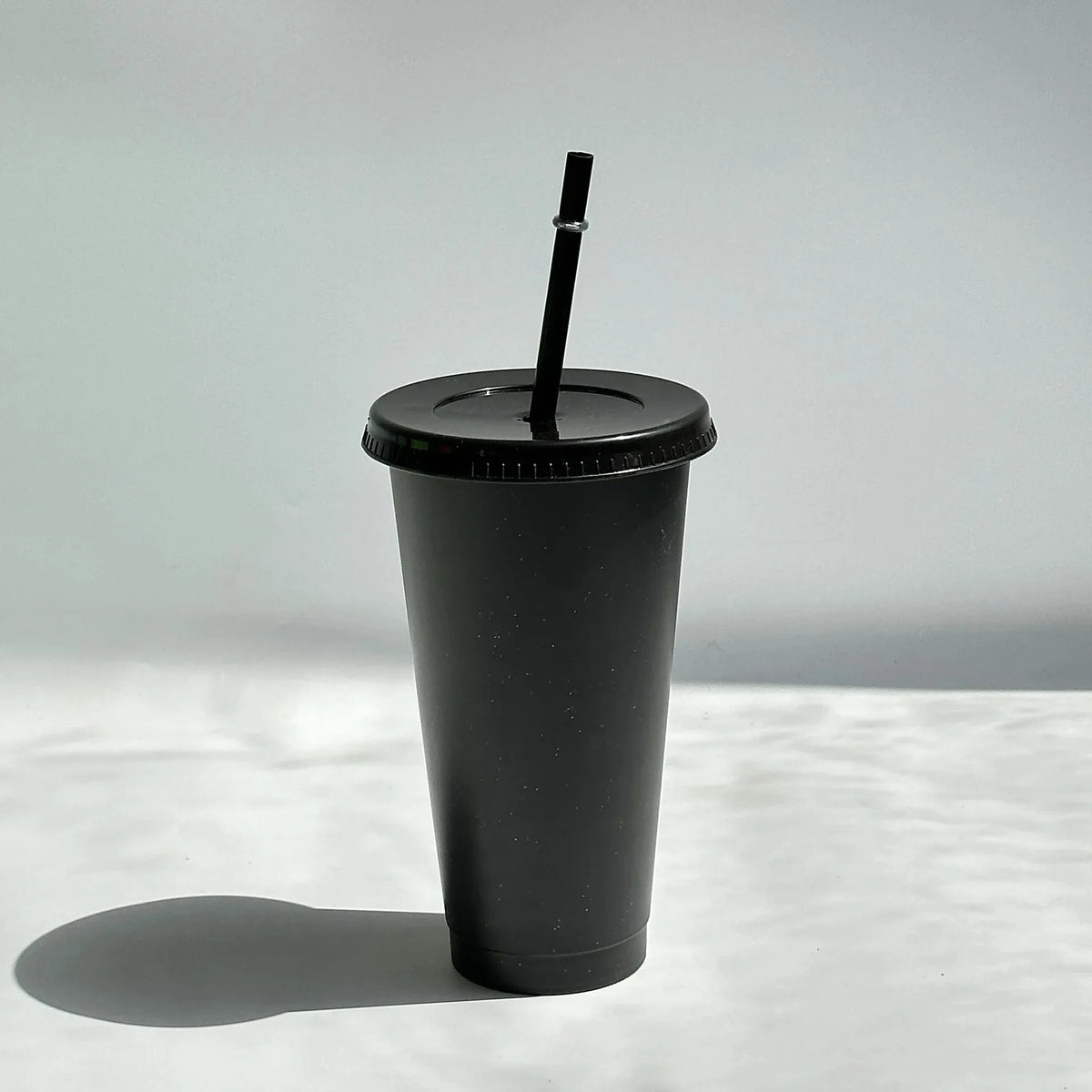 A black glitter party cup with a black lid and straw standing on a white surface.