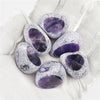 A cluster of tumbled amethyst crystals with purple and clear inclusions resting on white fabric.