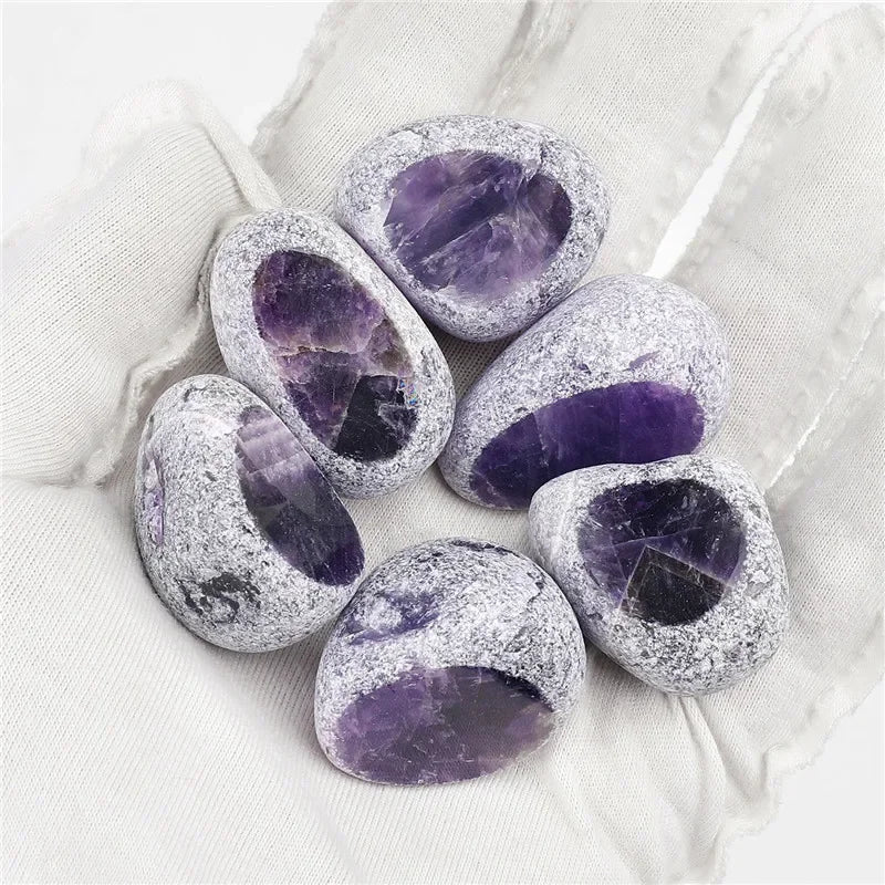 A cluster of tumbled amethyst crystals with purple and clear inclusions resting on white fabric.