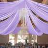 Purple sheer chiffon curtains draped overhead with a chandelier in an indoor event setting.