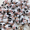 A collection of white and black handmade crochet cow keychains scattered on a white surface.