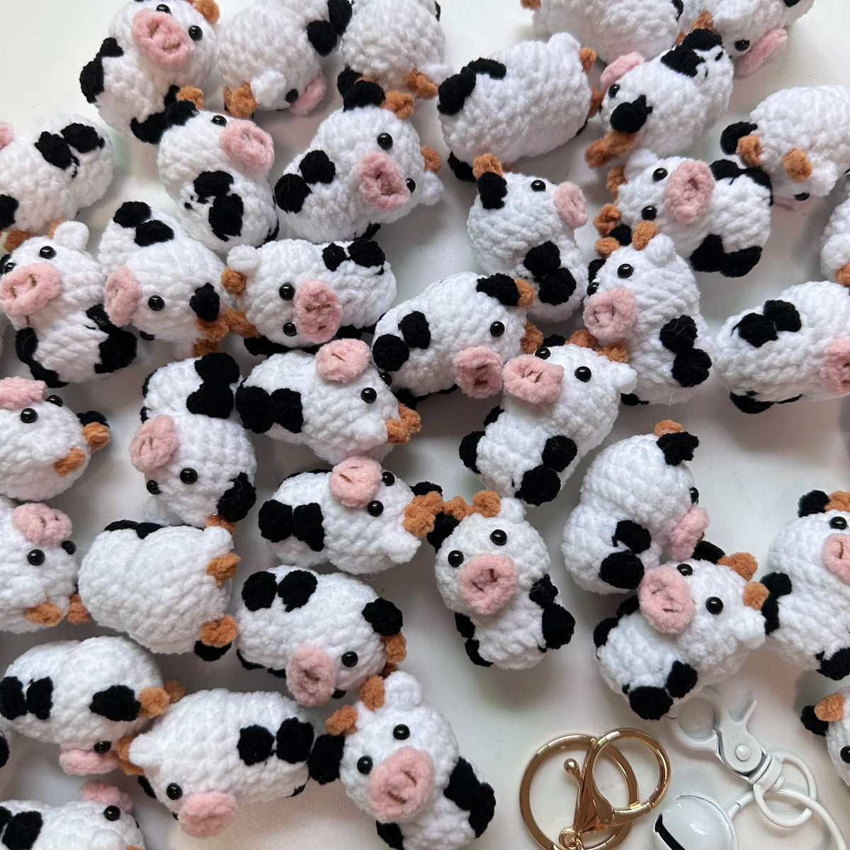 A collection of white and black handmade crochet cow keychains scattered on a white surface.