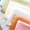 A stack of satin fabric in various colors including pale green, white, and peach tones.